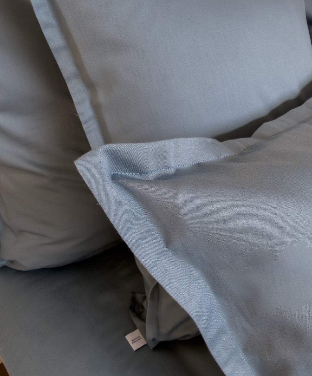 Lit fait avec une housse de couette en satin de coton bio bleu minéral, linge de lit fabriqué dans les Vosges