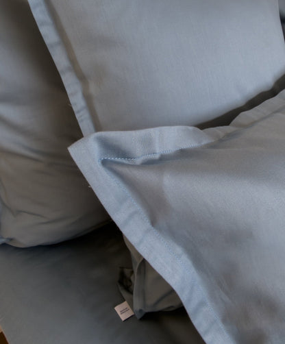 Lit fait avec une housse de couette en satin de coton bio bleu minéral, linge de lit fabriqué dans les Vosges 